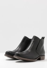Bottes cheville en cuir noir avec un bout arrondi, des panneaux élastiques sur les côtés et un petit talon en bois marron. Texture lisse avec des détails de couture minimaux.