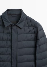Dunkelgraue gepolsterte Jacke mit Kragen, die ein gesticktes Muster und eine glatte Textur aufweist. Die Vorderseite hat einen verdeckten Verschluss und keine sichtbaren Beschläge.