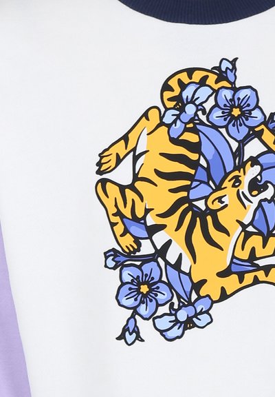 Sweatshirt en coton avec un corps blanc, des manches violettes et un graphisme de tigre jaune entouré de fleurs bleues, avec des contours audacieux.