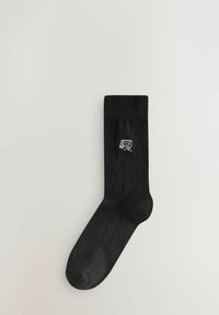 Calzino di cotone nero con polsino a costine e una piccola grafica a tema sportivo bianca che raffigura una porta e una palla. Texture liscia, design fino al ginocchio.
