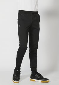 Svarte sweatpants med snor i taljen, sidelommer og ribbede manchetter; lavet af et blødt stof med en glat struktur.