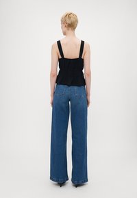 Svart peplum-bluse med brede stropper, kombinert med høyt liv, løstsittende blå denimjeans med klassisk 5-lommers design.
