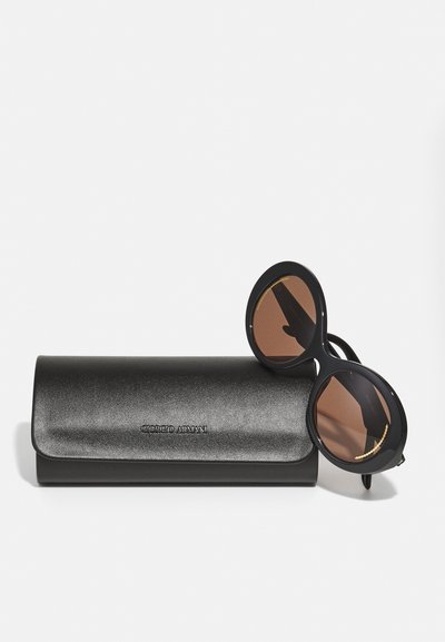 Black sunglasses with round lenses, brown tint, and gold accent. Accompanied by a black, textured leather case featuring embossed logo.