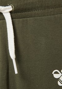 Olivgrön träningsbyxa i mjukt material, med en vit dragsko och en liten vit grafisk detalj på framsidan.