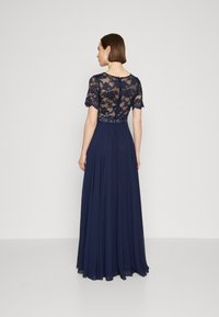 Pakaian malam biru navy dengan bodice renda yang memiliki lengan pendek, rok mengalir, dan hiasan manik-manik di pinggang.