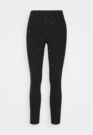 Jean skinny noir taille haute avec de petites broderies de roses rouges dispersées sur le tissu.