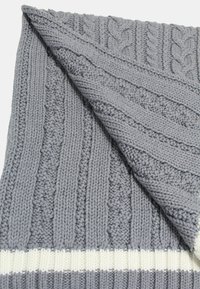 Plaid in maglia grigia con motivi testurizzati, caratterizzata da design a treccia e costine, e un bordo a strisce bianche. Materiale morbido e spesso in filato.