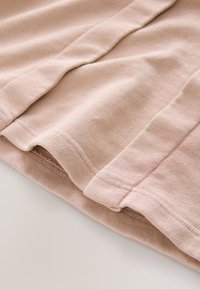 Šviesiai rožinė medvilninė medžiaga, minkšta tekstūra su briaunuota paviršiaus struktūra, turinti sulankstytas kraštines ir siūles. Subtilus, tvarkingas apdailos detalizavimas.