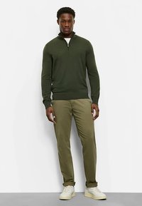 Olive green zip-neck sweater made of soft knit fabric, paired with light olive green pants and neutral-colored sneakers.