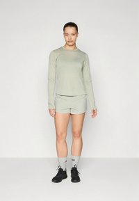 Világoszöld sportos hosszú ujjú póló hozzáillő rövidnadrággal. Kerek nyakkivágással rendelkezik, és könnyű, légáteresztő anyagból készült.