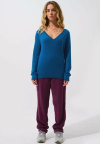 Blauer Woll-V-Ausschnittpullover mit langen Ärmeln, kombiniert mit lockeren, gerippten kastanienbraunen Hosen und grauen Turnschuhen. Einfacher, strukturierter Stoff.