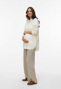 Pull en tricot écru avec des détails en côtes, associé à un pantalon large côtelé beige et des chaussures à lacets marron, porté par un mannequin enceinte.