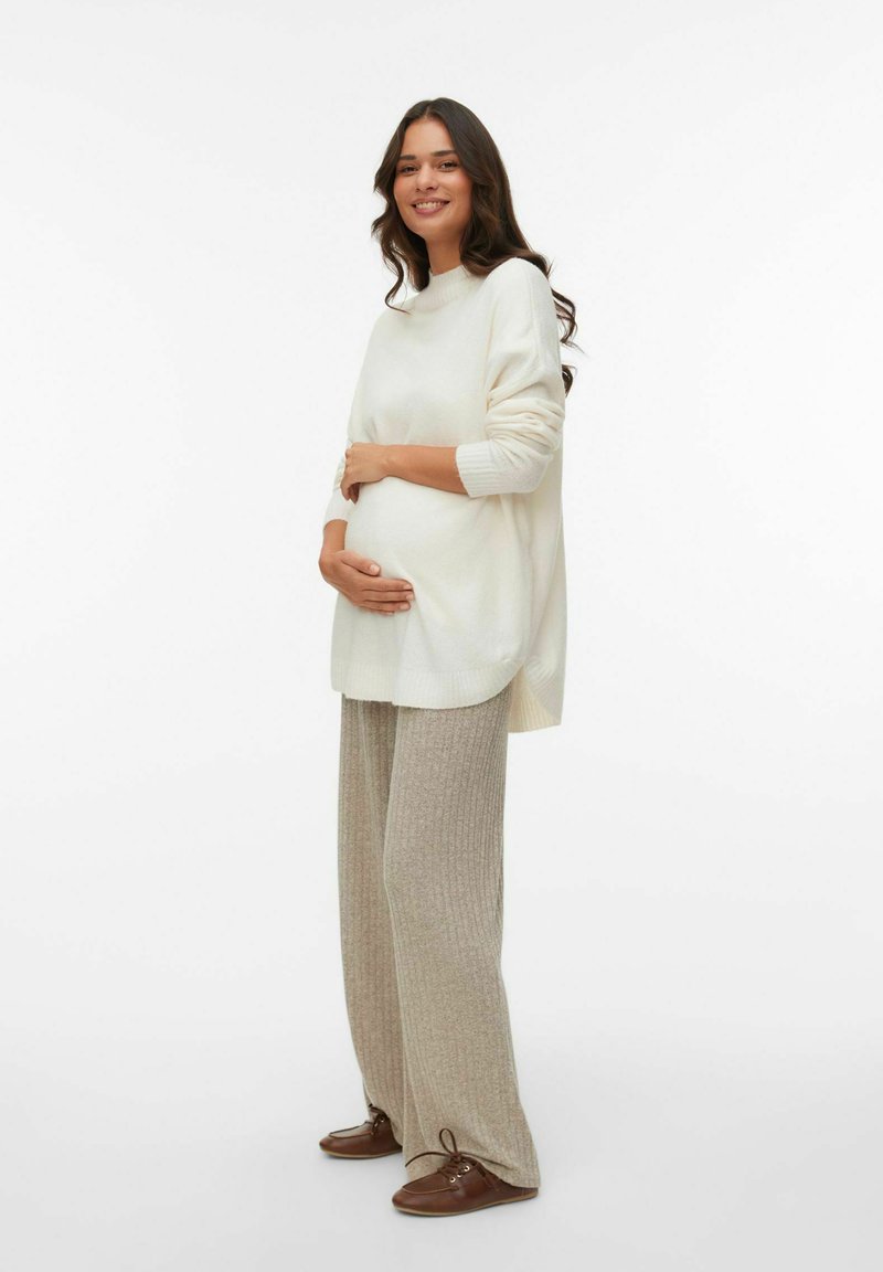 Pull en tricot écru avec des détails en côtes, associé à un pantalon large côtelé beige et des chaussures à lacets marron, porté par un mannequin enceinte.