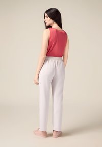 Débardeur en satin rouge, pantalon taille élastique gris clair en tissu doux, et baskets rose pastel. Modèle vu de dos.