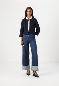 Het verkorte marineblauwe jack met een witte kraag, gecombineerd met hooggewaisted flared jeans met denim manchetten en zwarte puntige schoenen.