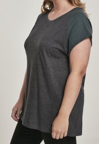 Camiseta gris oscuro con cuello redondo y mangas cortas en color verde azulado. La tela es suave, con un corte casual y una textura lisa.