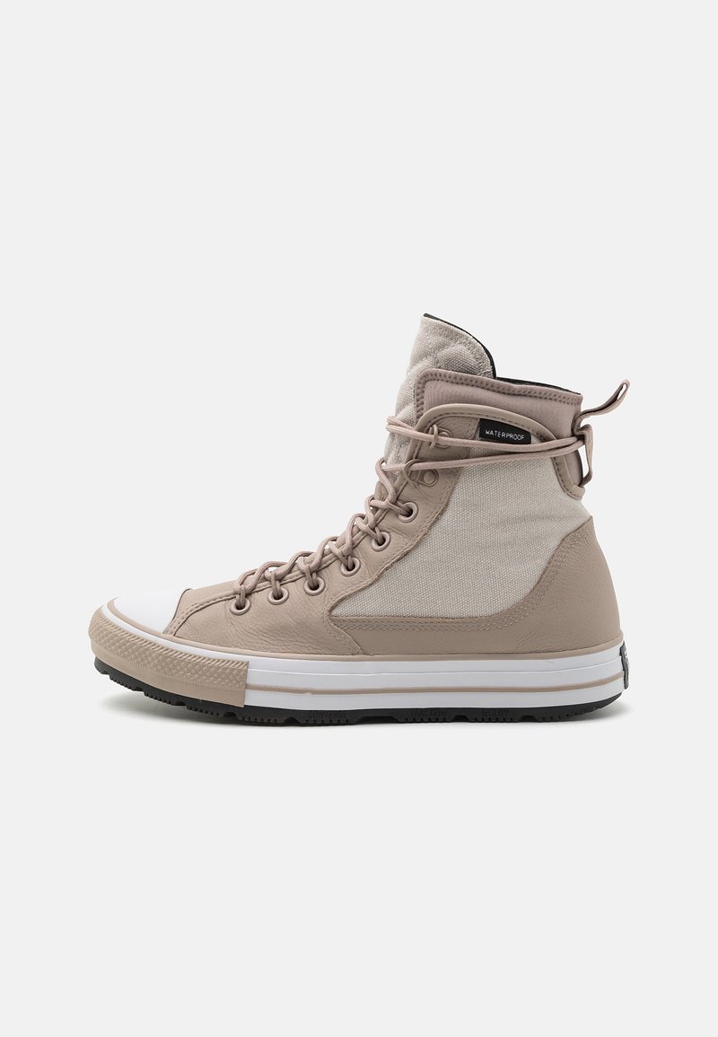 Beige a bílá voděodolná sneaker s vysokým střihem, šněrováním vpředu, textilními a koženými panely, bílou špičkou a silnou gumovou podrážkou.