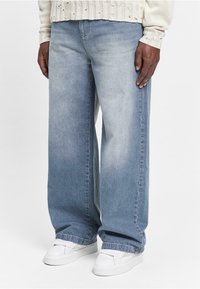 Lyseblå vide jeans i denim med en falmet finish, frynset kanter og fuldendt med hvide sneakers.