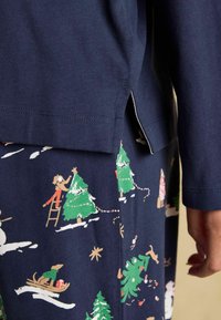 Tumedast sinine pika varrukaga särk külgmiste lõhikute ja mustriga tumeda kangaga, millel on jõulupuud, loomad ja pühade stseenid värvikates printides.