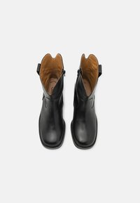 Botas de tobillo de cuero negro con acabado suave, abertura con forma de ondas, tirador trasero y un interior contrastante en color cuero, que cuenta con un cierre lateral.