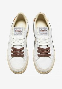 Sneaker bianche in pelle con lacci marroni, punta testurizzata e un accento in suede attorno alla suola. L'interno presenta una fodera a fantasia.