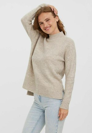 Light beige knitted sweater with a high collar, ribbed hem, and long sleeves. Paired with light blue jeans, displaying a relaxed fit.