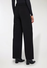 Pantaloni neri a gamba larga con vita elastica, realizzati in un tessuto morbido, caratterizzati da una superficie liscia e bordi orlati.