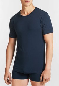 T-shirt a maniche corte di colore blu navy realizzato in materiale morbido, con scollo rotondo e design aderente. Indossato con biancheria intima blu navy coordinata.