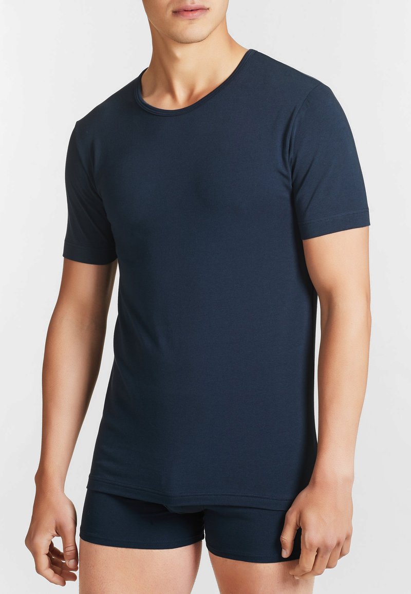 T-shirt a maniche corte di colore blu navy realizzato in materiale morbido, con scollo rotondo e design aderente. Indossato con biancheria intima blu navy coordinata.