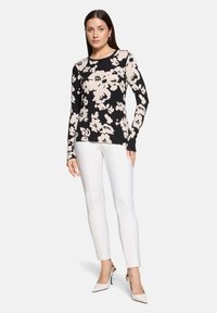 Czarna bluzka z długim rękawem w kremowy kwiatowy wzór, zestawiona z białymi dopasowanymi spodniami i białymi szpilkami w szpic. Gładka faktura materiału.