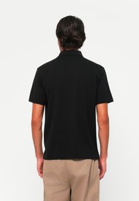 Sort polo-shirt med klassisk krave, korte ærmer og lige kant. Glat stof uden synlige mønstre eller detaljer.
