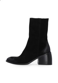 Schwarze Wildleder-Stiefelette mit runder Spitze, kurzem Schaft und einem leicht strukturierten Blockabsatz. Die glatte Oberfläche des Absatzes steht im Kontrast zum Obermaterial.