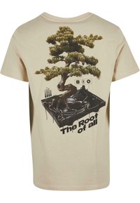 Cream short-sleeve t-shirt featuring a large graphic of a bonsai tree on a turntable, with the text "The Root of all" below.