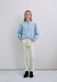 Blusa azul claro abotonada con mangas abullonadas y detalles bordados en blanco, combinada con jeans de pierna ancha color crema de talle alto y botas marrones hasta el tobillo.