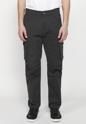 Schwarze Cargo-Hosen mit mehreren Seitentaschen, einer slim-fit Passform und einer glatten Textur, kombiniert mit schwarzen Sneakers auf einem schlichten Hintergrund.