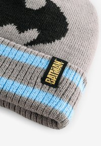 Grau gestrickte Beanie mit einem schwarzen Grafikdesign, hellblauen Streifen und einem schwarzen Etikett mit "Batman" in gelber Schrift. Weicher, strukturierter Stoff.