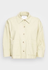 Ljust beige knäppjacka med krage, två framfickor och en texturerad tyg. Har rundade knappar och korta ärmar.