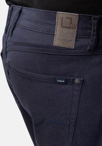 Dunkelblaue Hosen aus strukturiertem Stoff, mit grauem Logo-Patch, Steppnähten und Knopfverschluss. Enthält Gesäßtaschen.