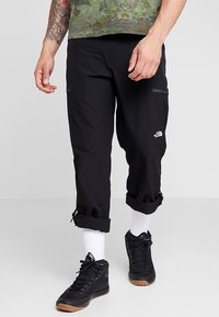 Mustat cargo-housut, jotka on valmistettu kestävästä materiaalista, joissa on käännetyt lahkeet, sivu-tasku vetoketjulla ja pieni logo alaosassa.