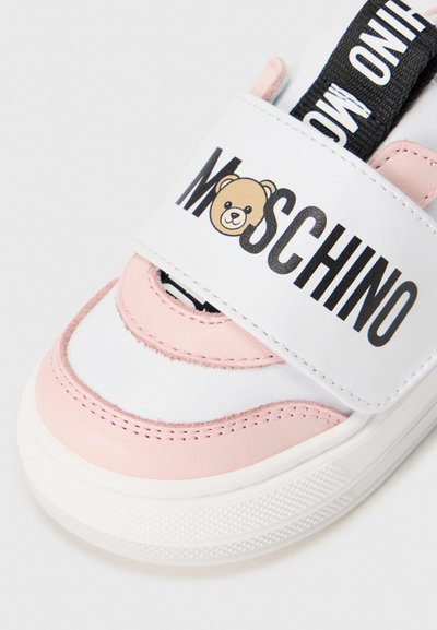 Baskets blanches et roses avec un graphique d'ours et le texte "Moschino" sur une bride. Matériau en cuir lisse, bout rond, semelle texturée.