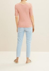 Světle růžový top s krátkým rukávem a kulatým výstřihem, spárovaný se světle modrými džíny po kotníky s třásněmi a nazouvacími botami.