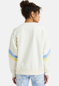 Cream-colored sweatshirt with blue and yellow stripes on the sleeves. Features a relaxed fit and textured fabric.