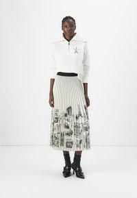 White zip-up sweatshirt with short collar, paired with a pleated black and white skirt featuring architectural sketches. Black heeled shoes.