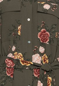 Olivengrünes Blumenhemd aus strukturiertem Stoff, mit rosa, kastanienbraunen und gelben Rosen, zwei Taschen und einem gebundenen Gürtel-Detail.