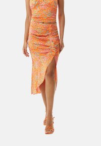 Orange floral print maxi skirt with a high slit, ruched detailing, and a smooth texture. Worn with matching orange strappy sandals.