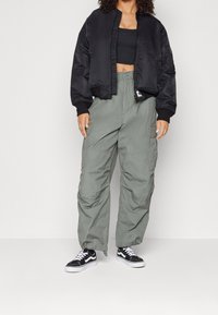 Zwarte bomberjack, verkort ontwerp, ribgebreide manchetten; olijfgroene cargobroek, losse pasvorm met zakken; zwart-witte Vans sneakers.