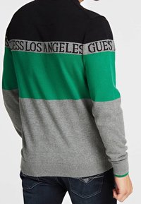 Maglione lavorato a maglia verde, nero e grigio con una fascia che presenta il testo "GUESS LOS ANGELES" sulla parte anteriore. Polsini e orlo a costine.