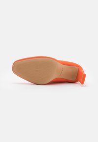 Chaussure à talon haut en daim orange avec un bout pointu, semelle intérieure texturée, et semelle en caoutchouc beige avec des stries pour plus d'adhérence.