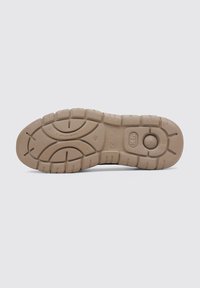 Semelle de chaussure en caoutchouc beige avec des motifs de grip texturés et un accent circulaire surélevé près du talon, présentant une finition lisse et mate.