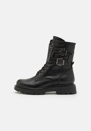 Black leather ankle boot with a rounded toe, lace-up front, two buckles, and metallic studs on a textured panel. Chunky sole design.